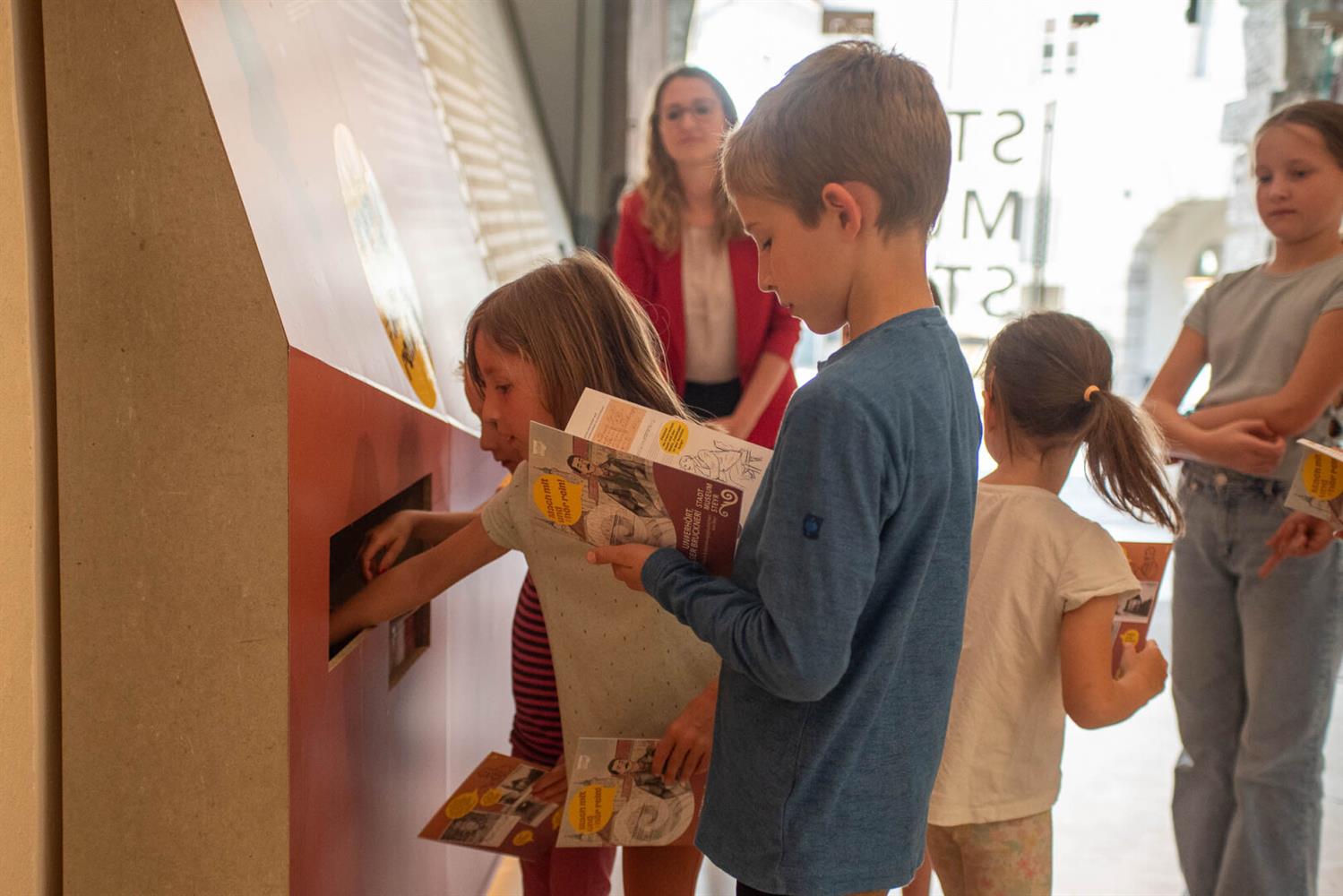 Kinder holen sich das Aktionsheft zur Ausstellung "UN#ERHÖRT, dieser Bruckner!" ab